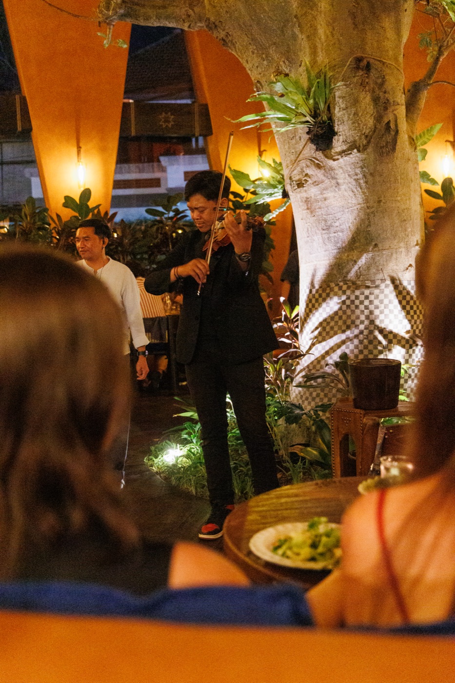A violinist playing between tables beside the tree at Jannah during Thursday violin night